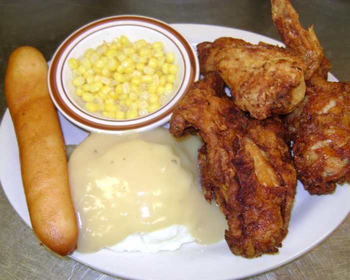A plate of broasted chicken with mashed potatoes and gravy, sweetcorn in a side bowl and a breadstick.