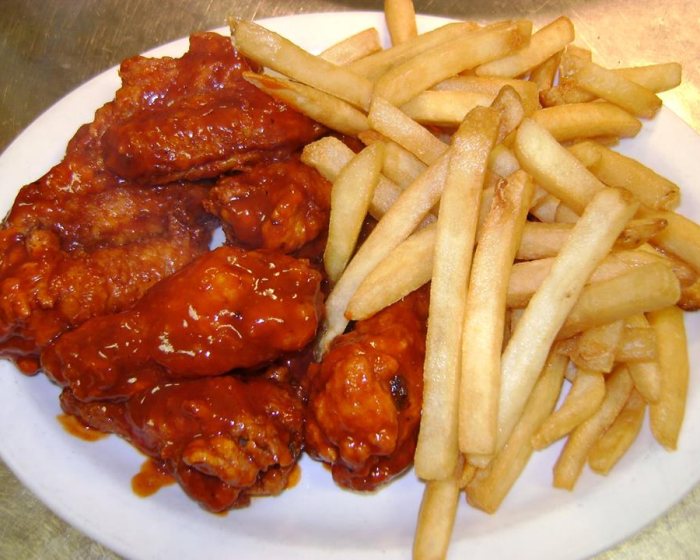 A plate of sauced wings piled beside a heap of french fries.