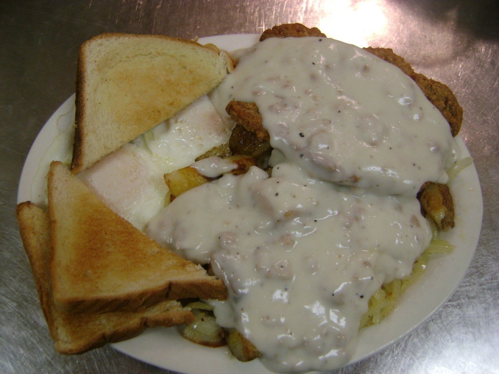 Country fried steak under sausage gravy with eggs, fried potatoes and toast.