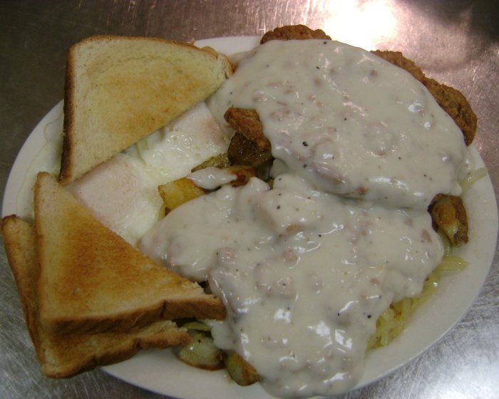 Country fried steak under sausage gravy with eggs, fried potatoes and toast.