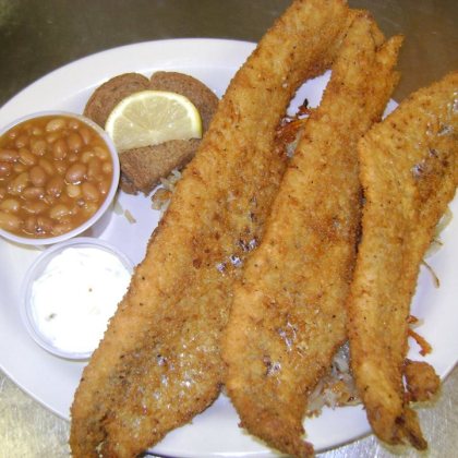 Three hand-breaded fish fillets over fried potatoes, with baked beans, homemade tartar sauce, dark rye bread and a lemon slice.