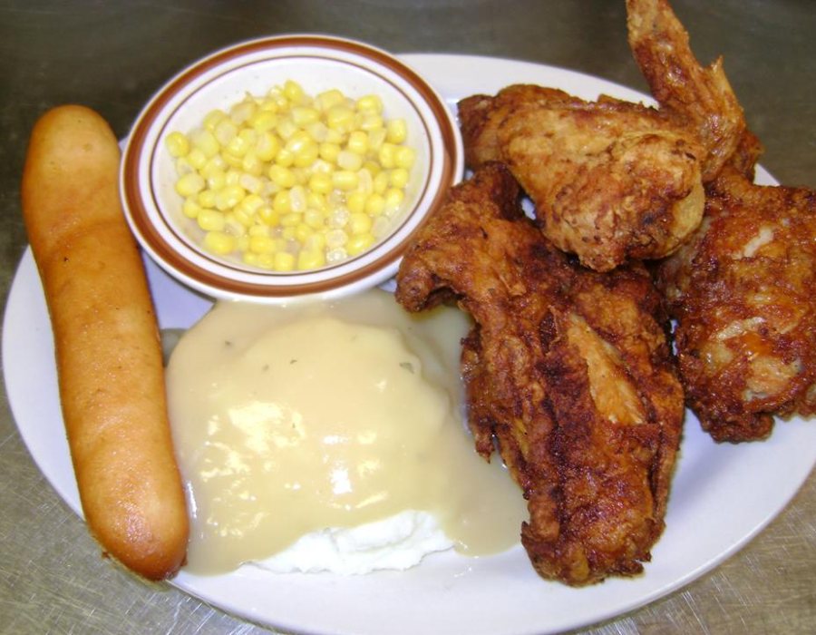 A plate of broasted chicken with mashed potatoes and gravy, sweetcorn in a side bowl and a breadstick.