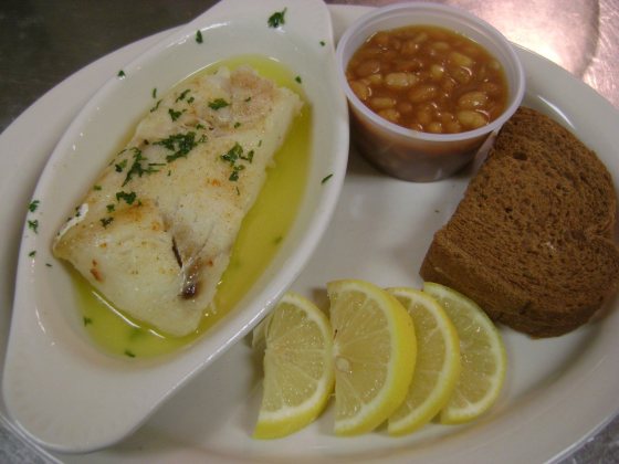Baked cod in butter with parsley, a cup of baked beans, dark rye bread and four lemon wedges.