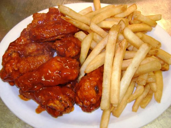 A plate of sauced wings piled beside a heap of french fries.