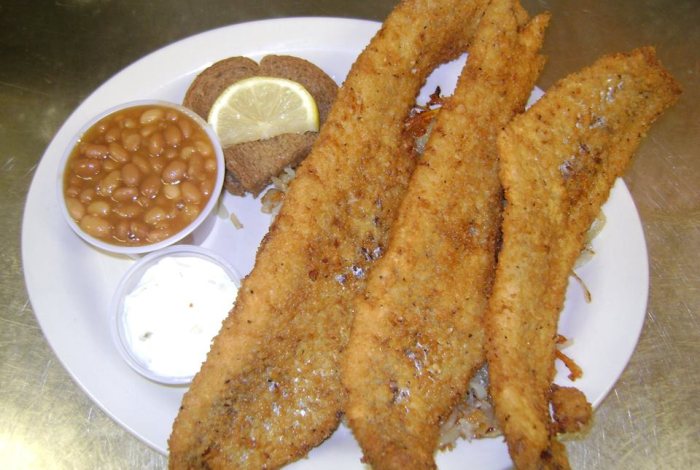 Three hand-breaded fish fillets over fried potatoes, with baked beans, homemade tartar sauce, dark rye bread and a lemon slice.
